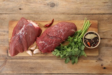 Photo of Pieces of raw beef meat, parsley, garlic and spices on wooden table, top view