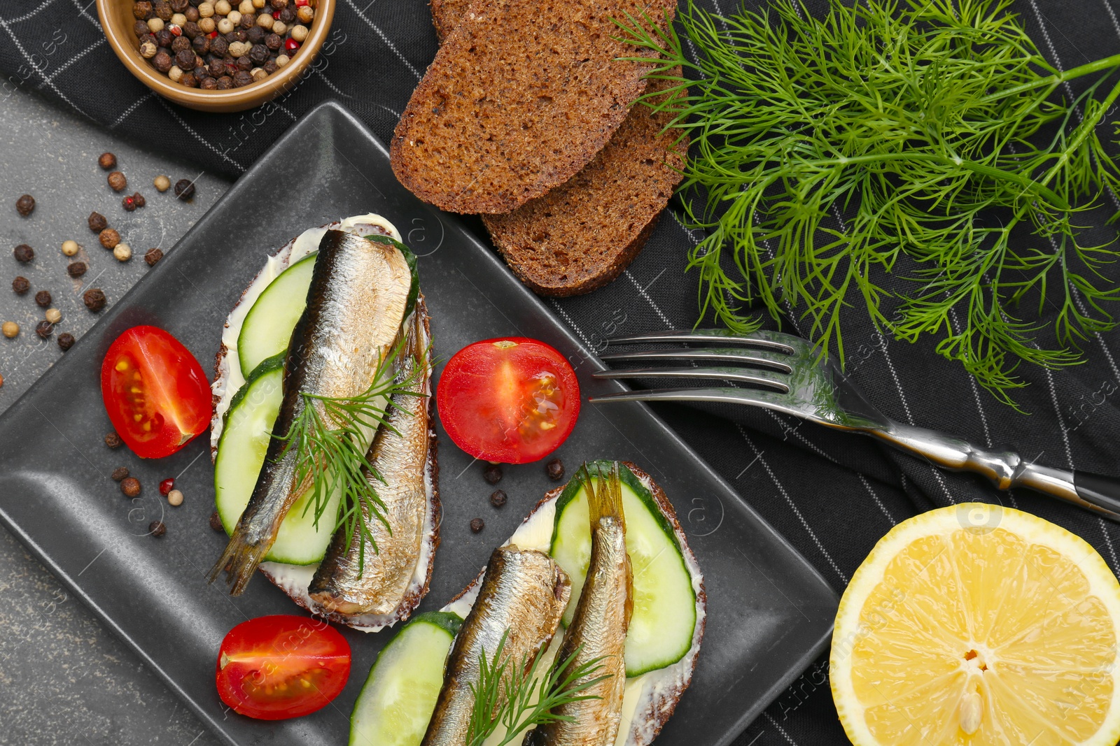 Delicious sandwiches with sprats, cucumber and dill served on grey table, flat lay Photo of Delicious sandwiches with sprats, cucumber and dill served on grey table, flat lay