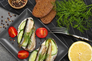 Photo of Delicious sandwiches with sprats, cucumber and dill served on grey table, flat lay