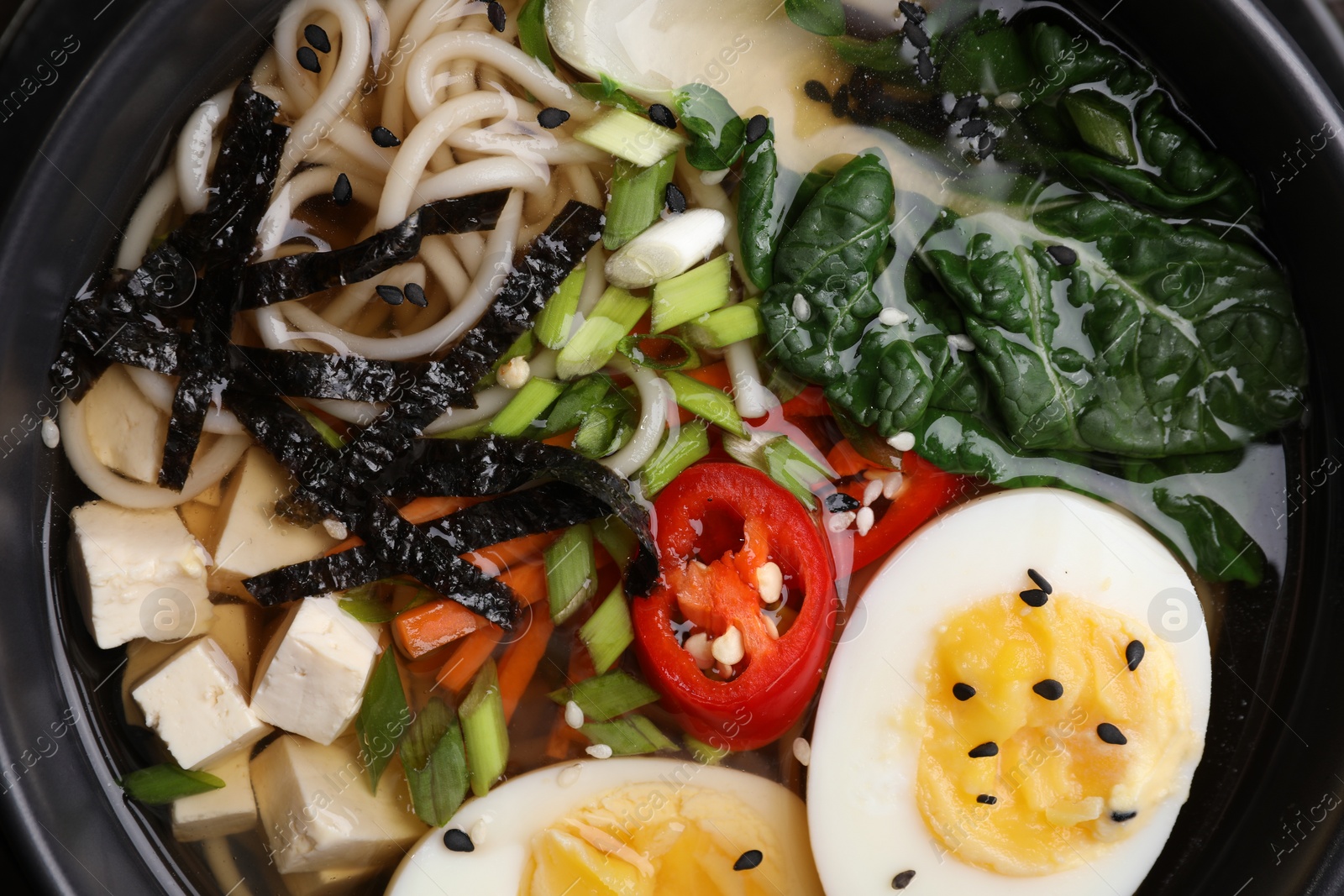 Photo of Delicious vegetarian ramen with egg, tofu and vegetables in bowl, top view. Noodle soup