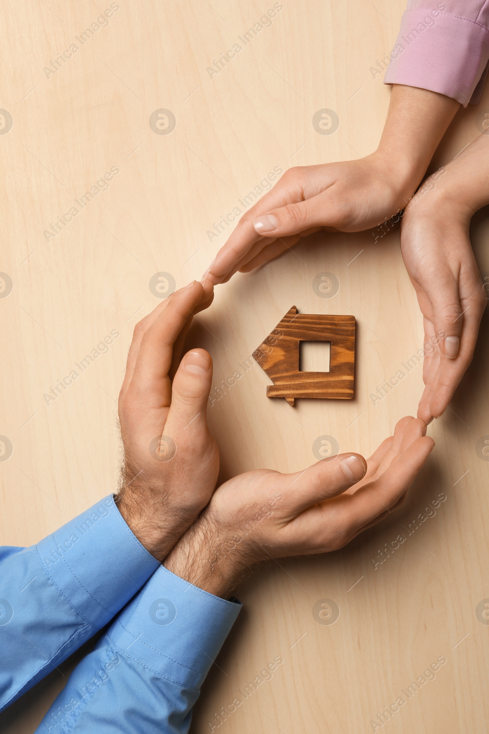 Photo of Couple holding hands near figure of house on wooden background, top view. Home insurance