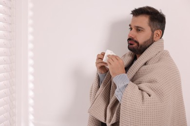 Photo of Sick man wrapped in blanket with tissue indoors, space for text. Cold symptoms