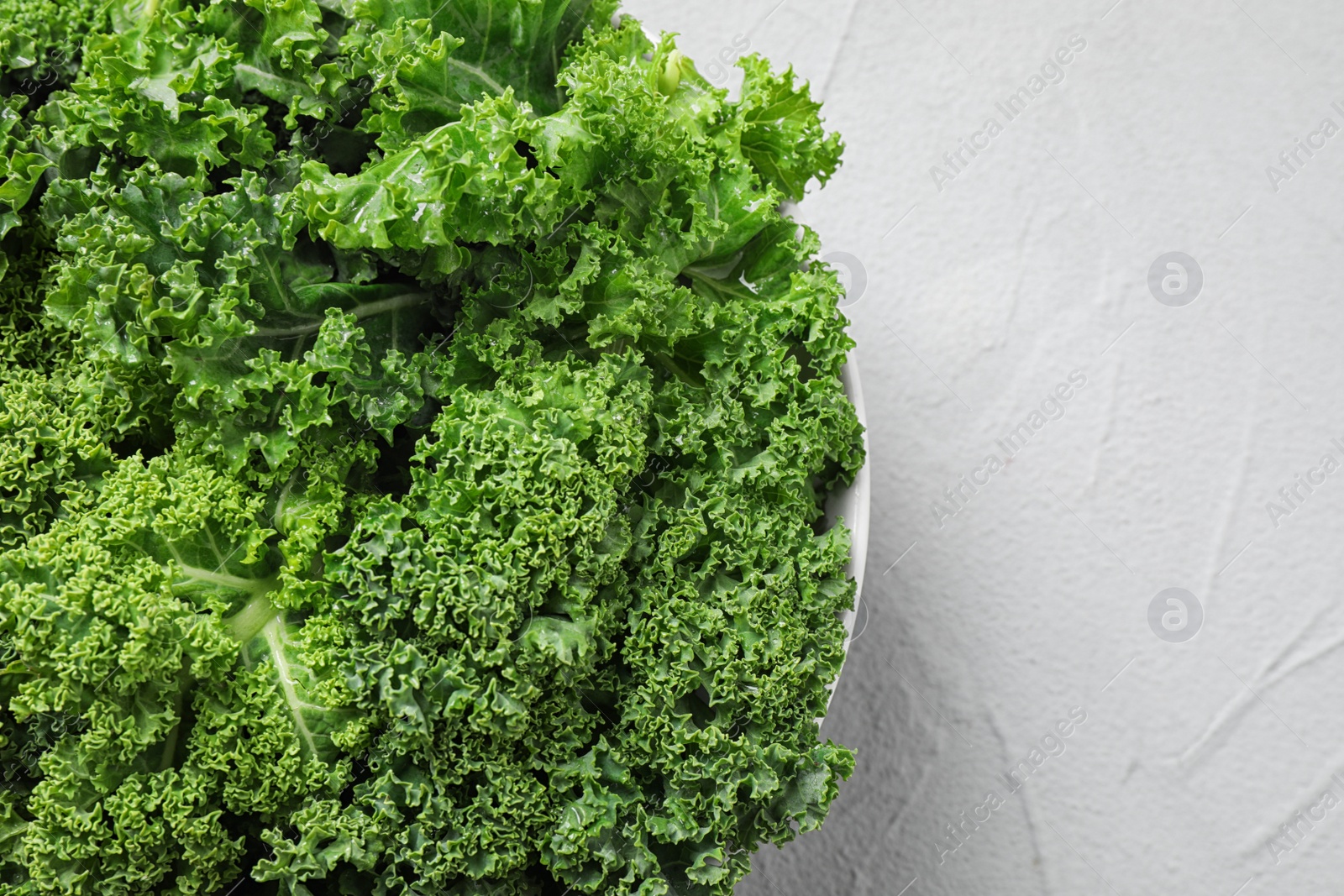 Photo of Fresh kale leaves on white table, top view. Space for text