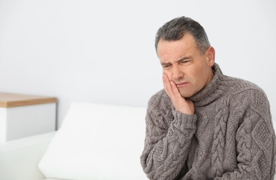 Mature man suffering from strong tooth pain at home, space for text