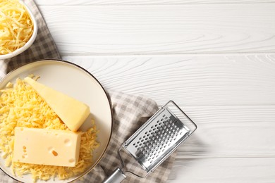 Photo of Grated, whole pieces of cheese and grater on white wooden table, flat lay. Space for text