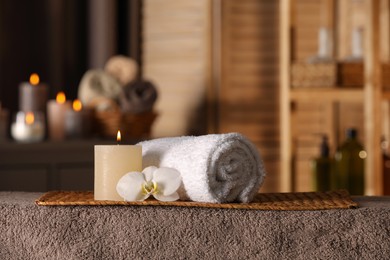 Photo of Spa composition with candle, orchid flower and rolled towel on massage table in wellness center, space for text