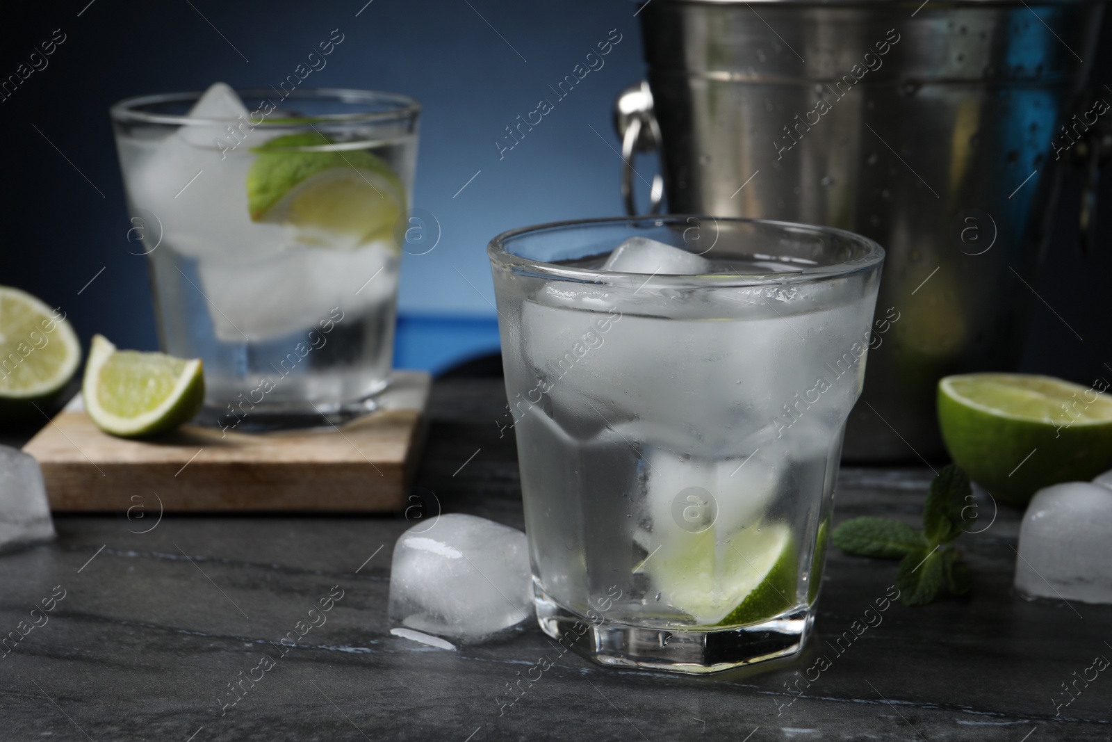 Photo of Glasses of vodka, lime, mint and ice on black marble table