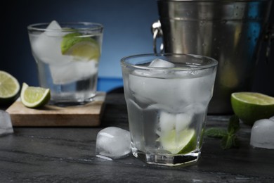 Photo of Glasses of vodka, lime, mint and ice on black marble table