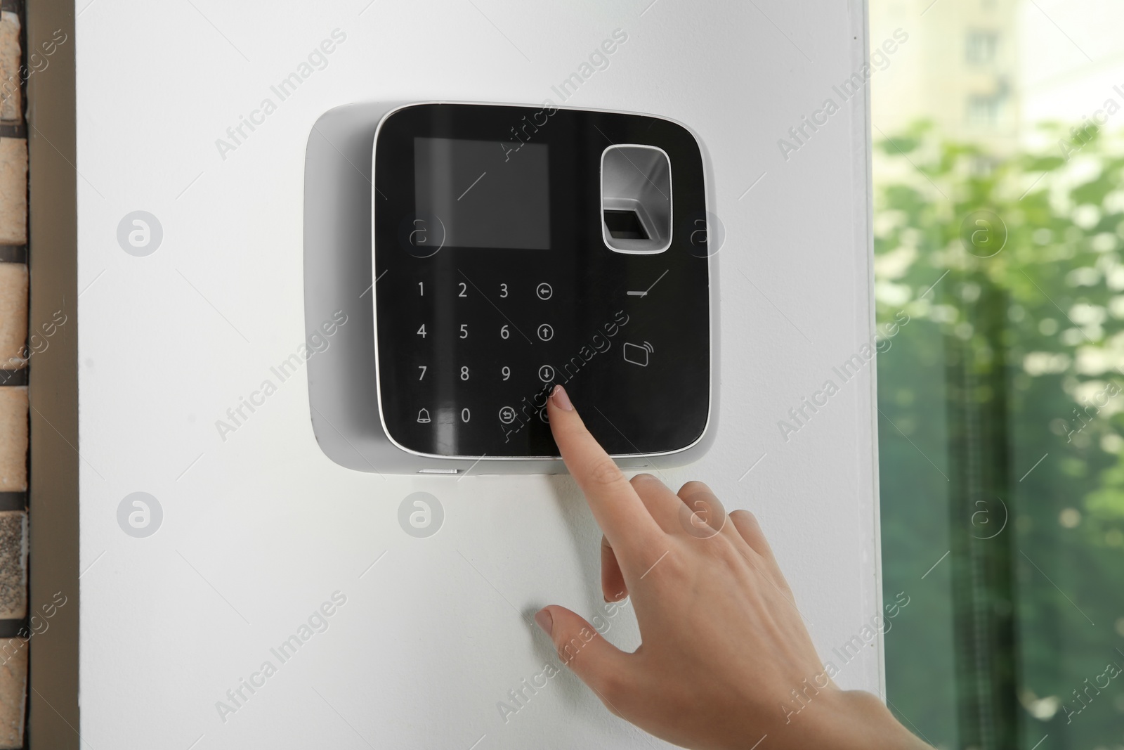 Photo of Young woman entering code on alarm system keypad indoors