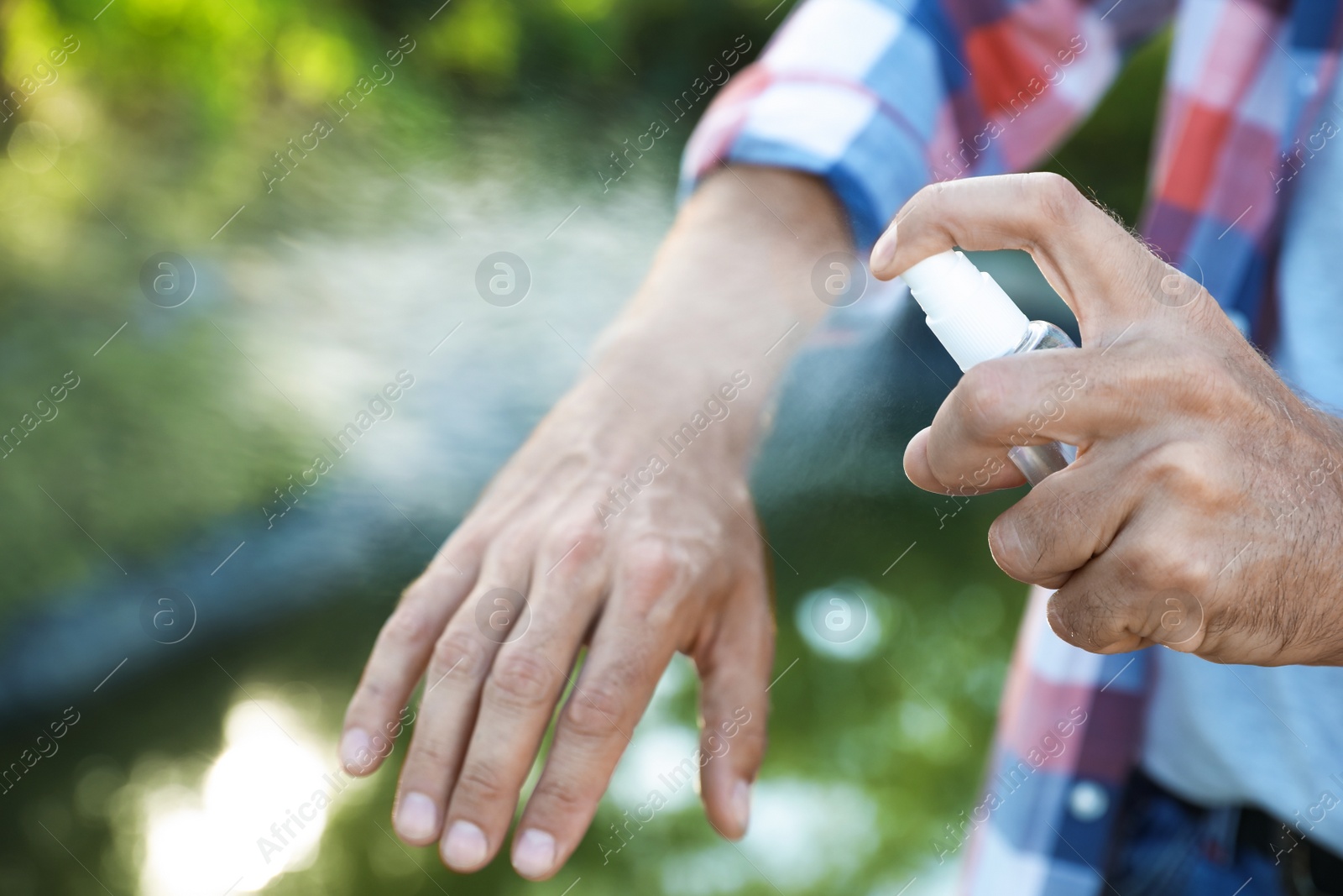 Photo of Man applying insect repellent onto hand outdoors, closeup