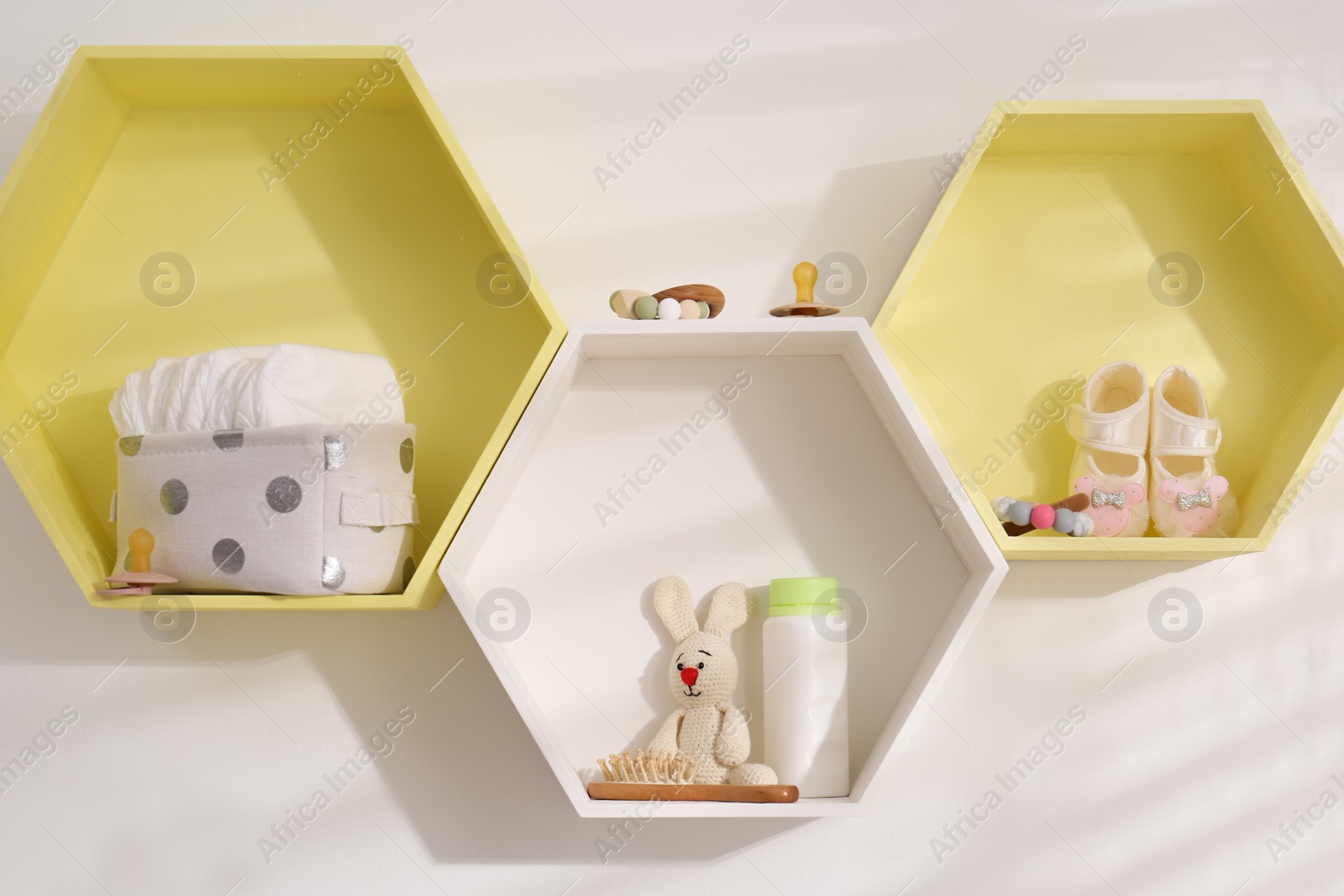 Photo of Hexagon shaped shelves with toys and child's accessories on white wall. Interior design