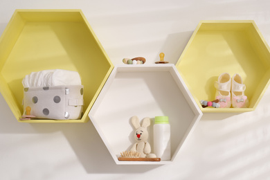 Photo of Hexagon shaped shelves with toys and child's accessories on white wall. Interior design
