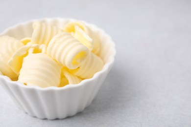 Photo of Tasty butter curls in bowl on light grey table, closeup. Space for text