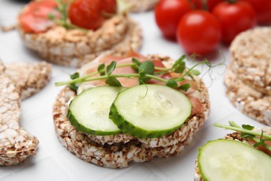 Photo of Crunchy buckwheat cakes with prosciutto, cucumber slices and greens on white table, closeup