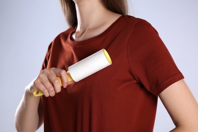 Woman cleaning red t-shirt with lint roller on grey background, closeup