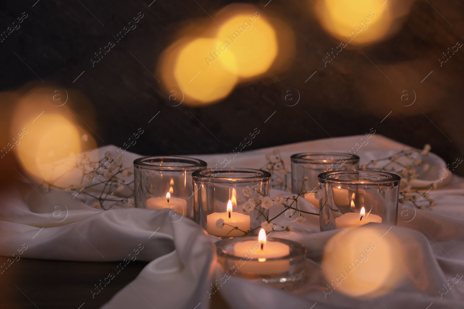 Photo of Burning candles and flowers on table against blurred festive lights