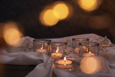 Photo of Burning candles and flowers on table against blurred festive lights