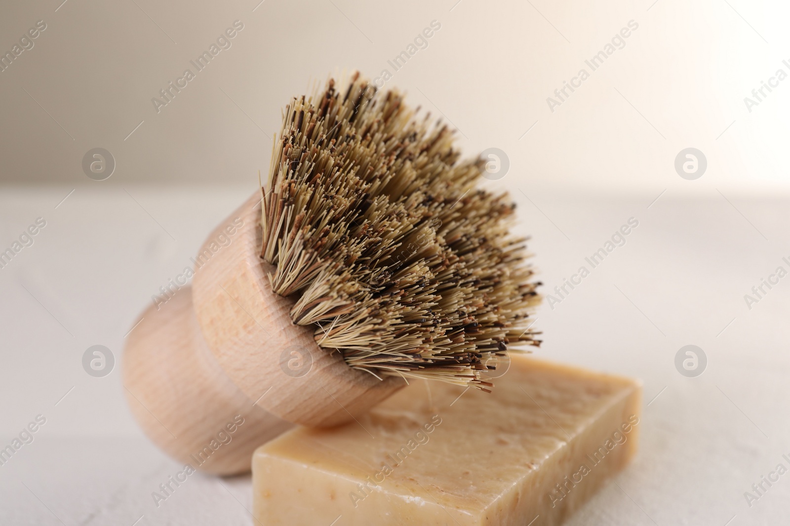 Photo of One cleaning brush and bar of soap on white textured table, closeup