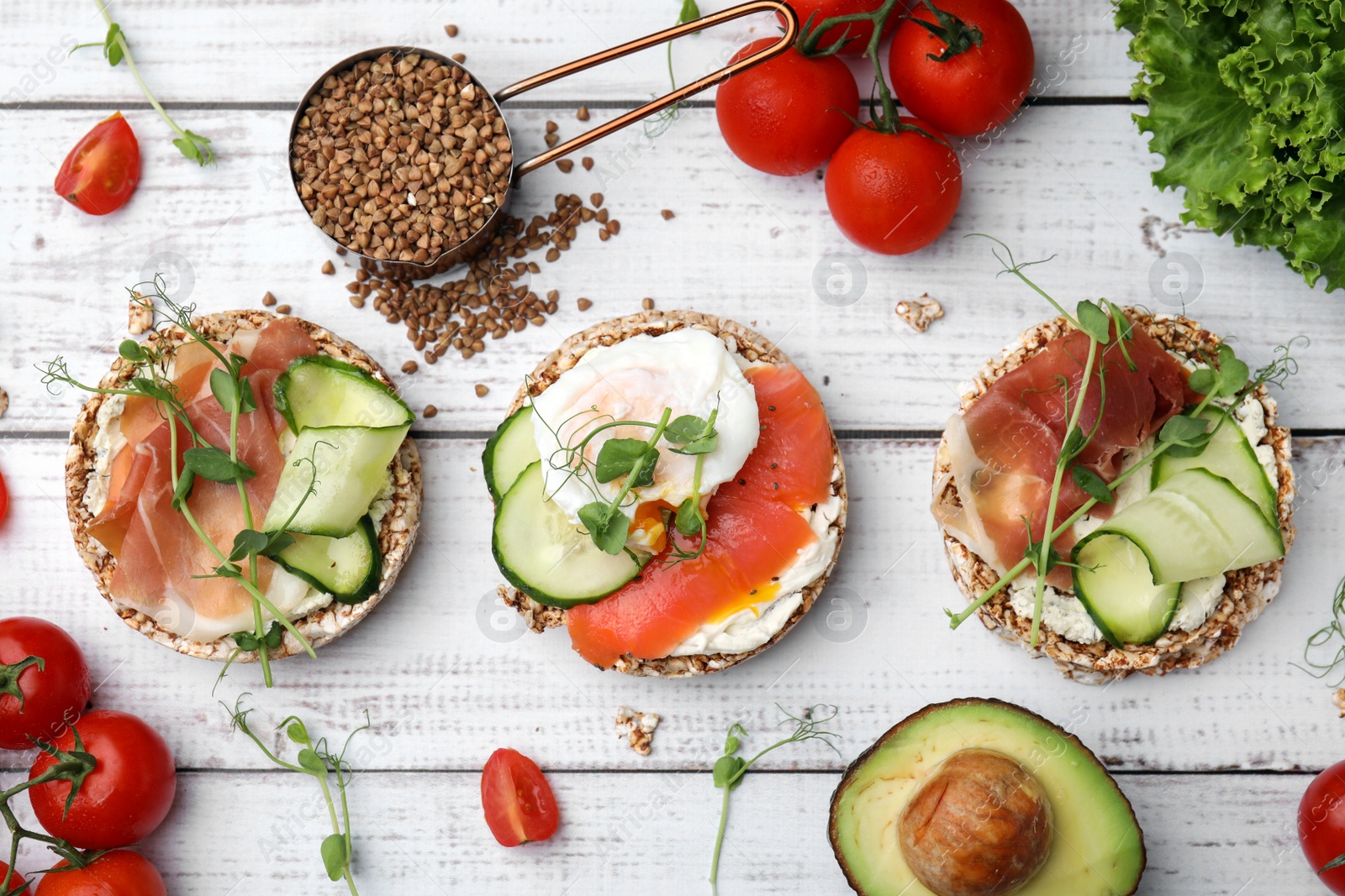 Photo of Set of crunchy buckwheat cakes with different ingredients on white wooden table, flat lay