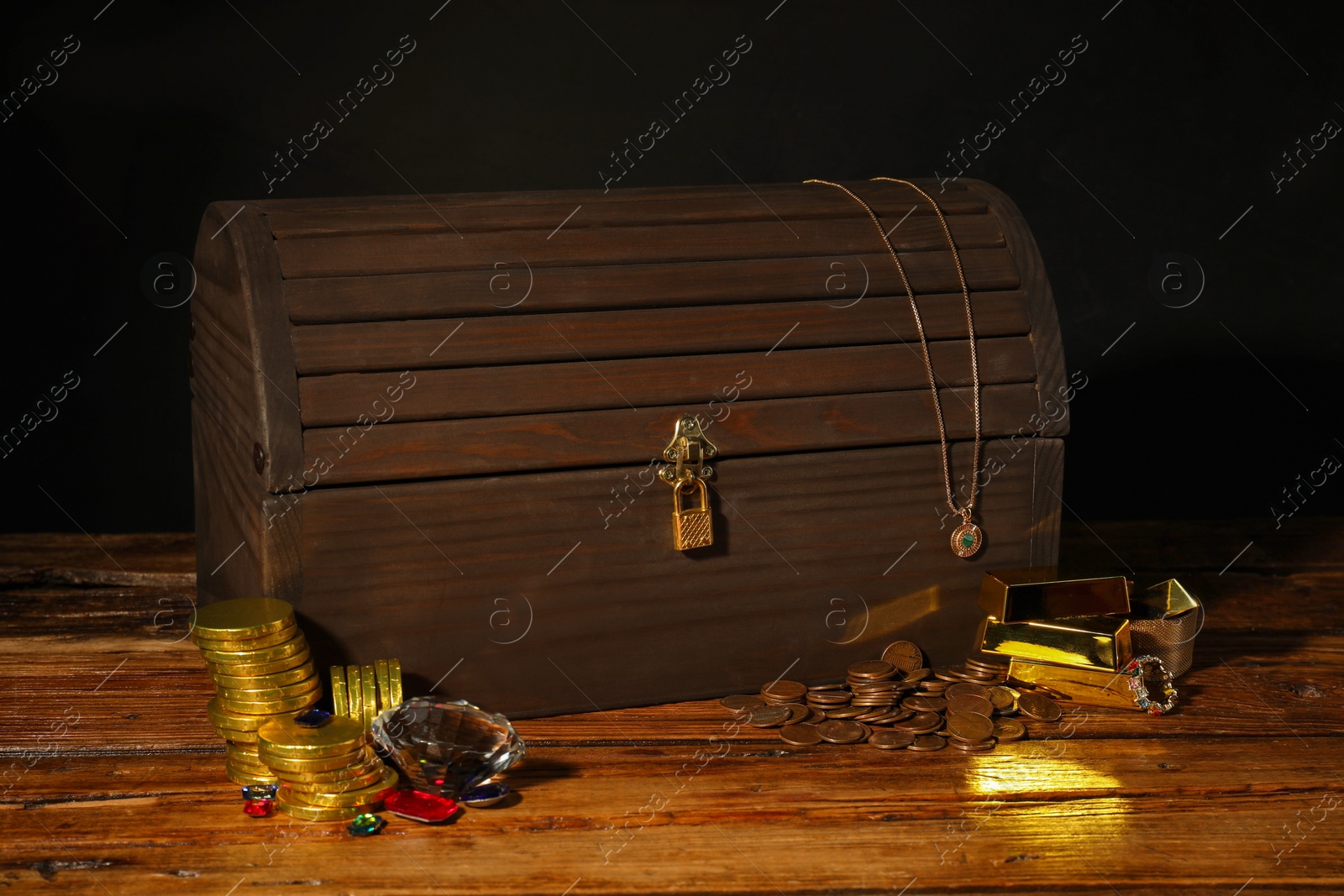 Photo of Treasure chest, gold bars, coins, jewelry and gemstones on wooden table