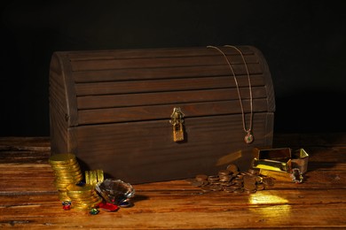 Photo of Treasure chest, gold bars, coins, jewelry and gemstones on wooden table