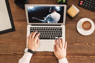 Image of Man watching performance of motivational speaker on laptop at wooden table, top view