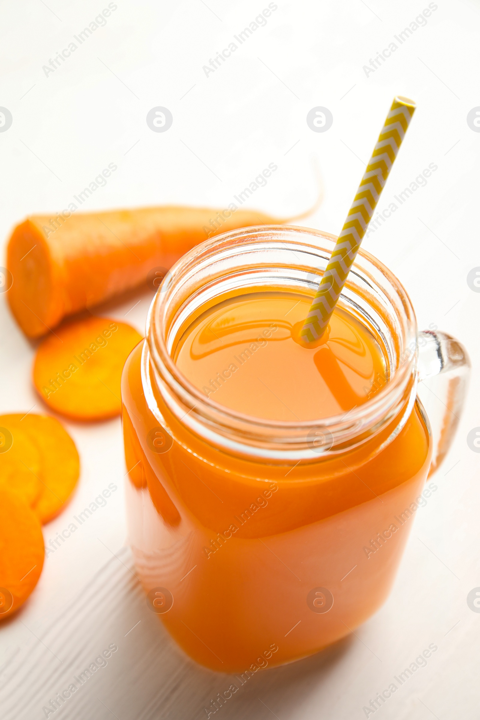 Photo of Freshly made carrot  juice in mason jar on white wooden table, closeup