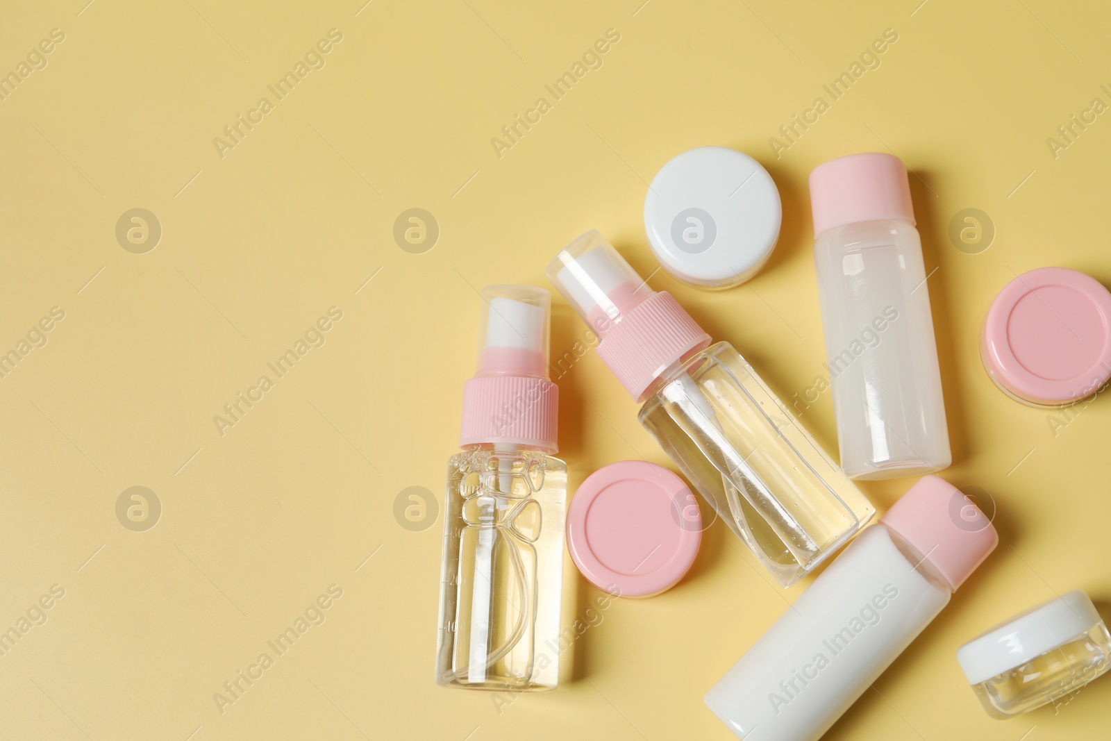 Photo of Cosmetic travel kit. Small containers of personal care products on yellow background, flat lay. Space for text