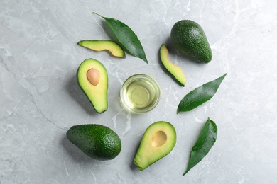 Bowl of natural oil and avocados on grey stone background, flat lay