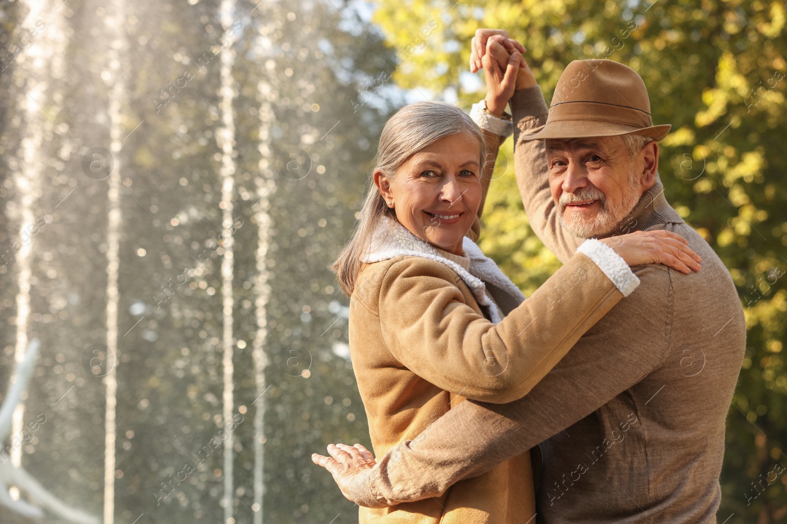 Photo of Affectionate senior couple dancing together near fountain outdoors, space for text