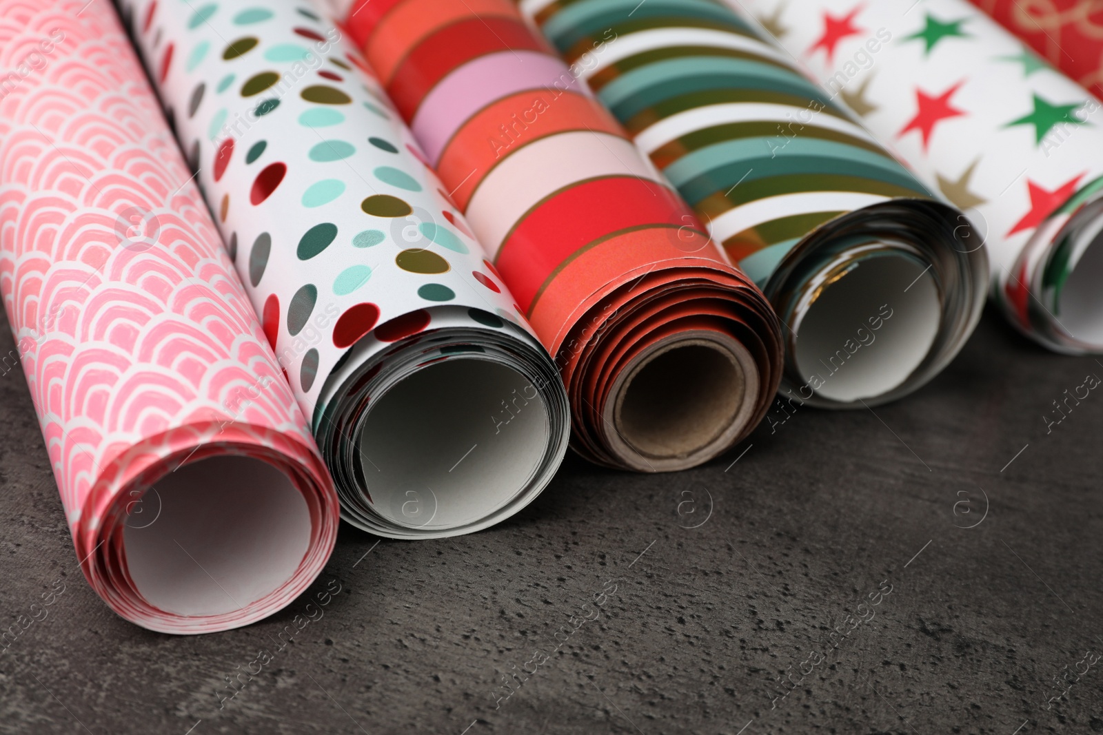 Photo of Different colorful wrapping paper rolls on grey table, closeup