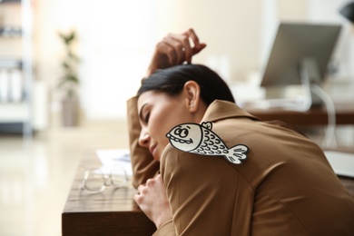 Photo of Man sticking paper fish to colleague's back while she sleeping in office, closeup. Funny joke