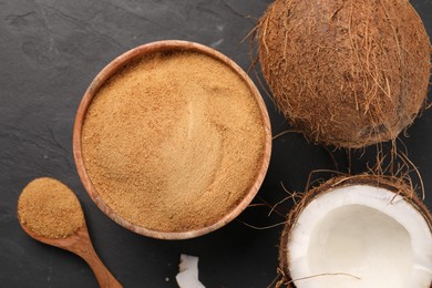 Photo of Spoon with coconut sugar, bowl and fruits on dark textured table, flat lay