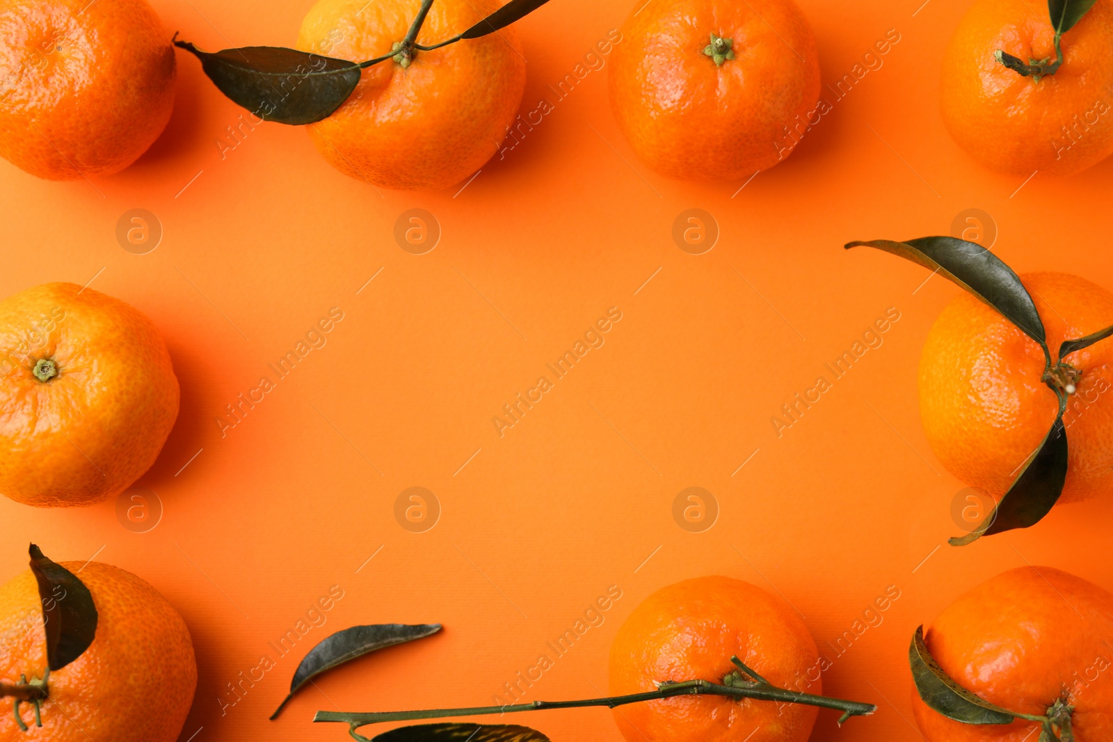 Photo of Frame made of many fresh ripe tangerines with green leaves on orange background, flat lay. Space for text