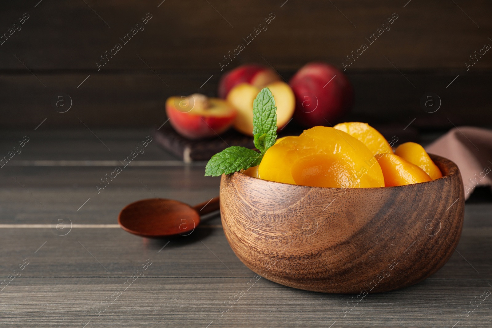 Photo of Canned peach halves in bowl on wooden table, space for text