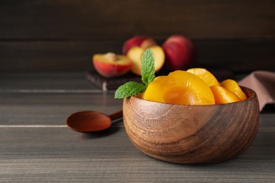 Canned peach halves in bowl on wooden table, space for text