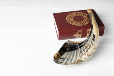 Photo of Shofar and Torah on white wooden table, space for text. Rosh Hashanah holiday symbols