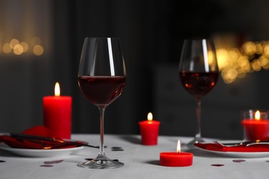 Photo of Romantic table setting with glasses of red wine and burning candles against blurred lights
