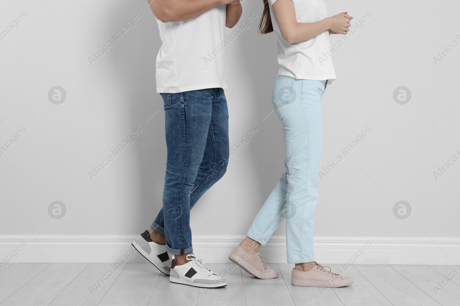 Photo of Young couple in stylish jeans near light wall, closeup