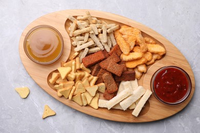 Photo of Wooden tray with different crispy rusks and dip sauces on light marble table, flat lay