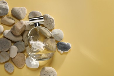 Bottle of luxury perfume in sunlight and stones on golden background, flat lay. Space for text
