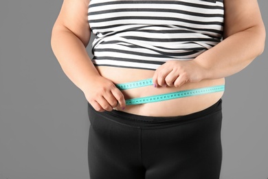 Overweight woman with measuring tape on gray background, closeup