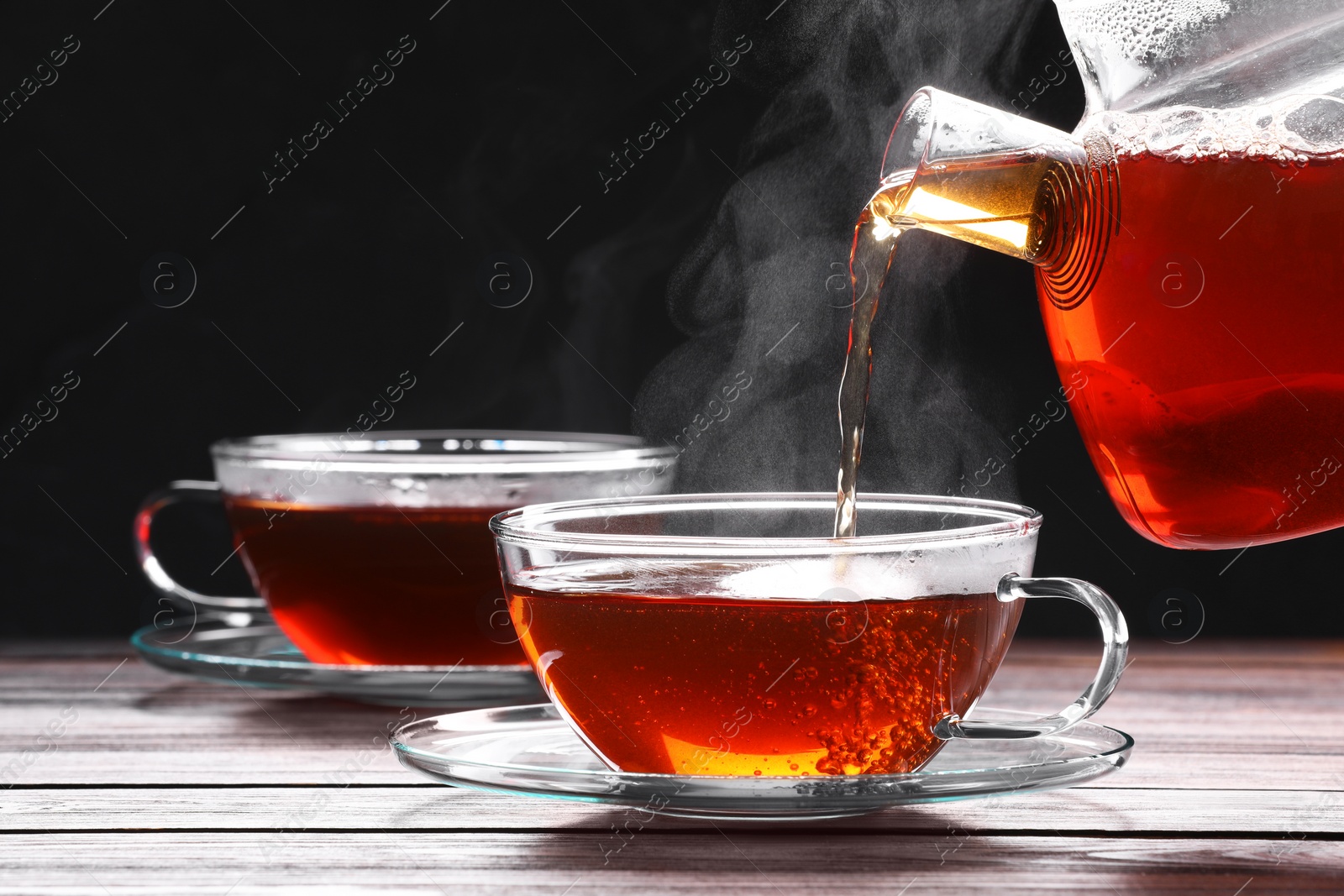 Photo of Pouring tea into glass cup on wooden table against black background, space for text