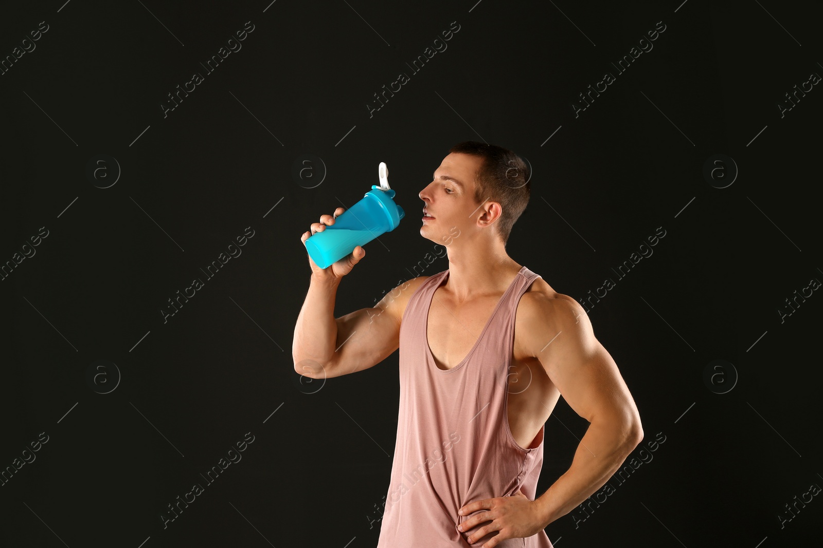 Photo of Athletic young man drinking protein shake on black background
