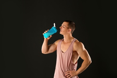 Photo of Athletic young man drinking protein shake on black background
