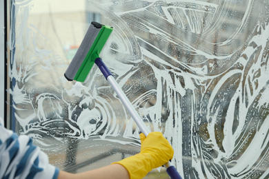 Woman cleaning window with squeegee at home, closeup. Space for text