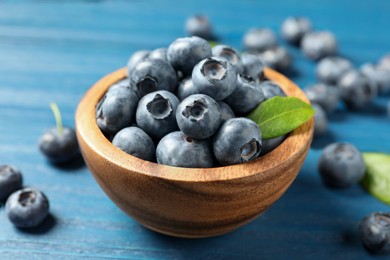 Photo of Bowl of fresh tasty blueberries on blue wooden table, closeup