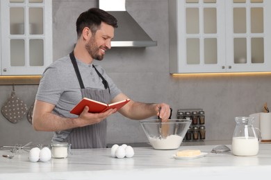 Happy man cooking by recipe book in kitchen
