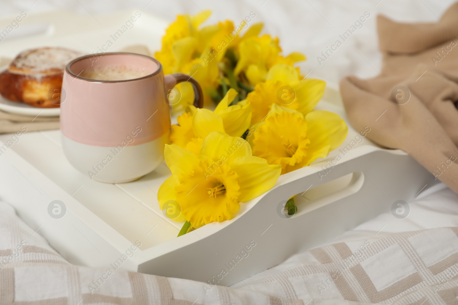 Photo of Bouquet of beautiful daffodils and coffee on bed, closeup