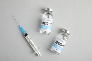 Vials with coronavirus vaccine and syringe on light background, flat lay